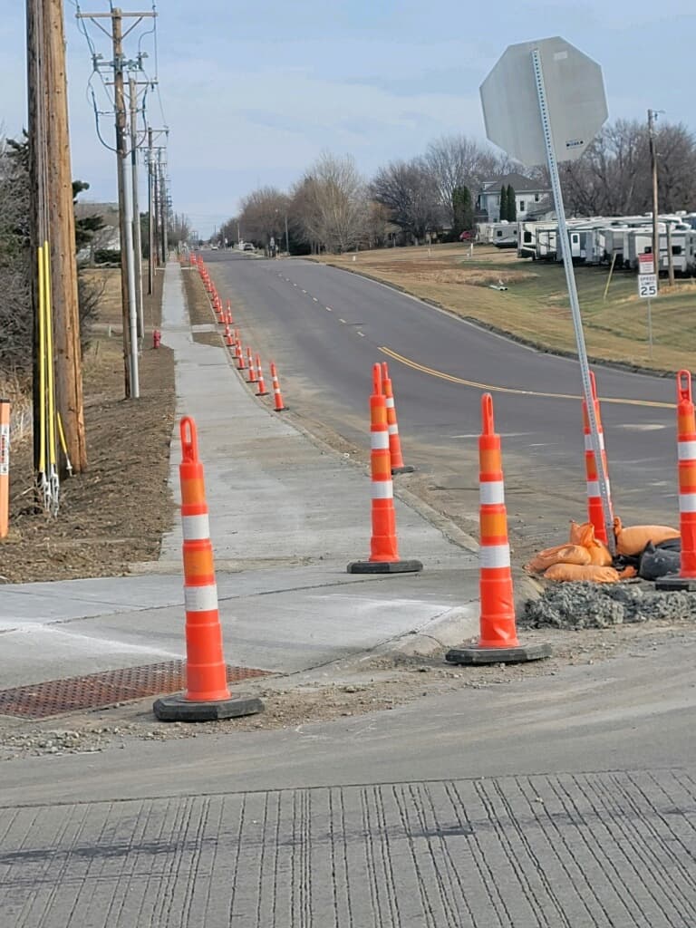 New city sidewalk and a curb ramp taking shape behind the cones
