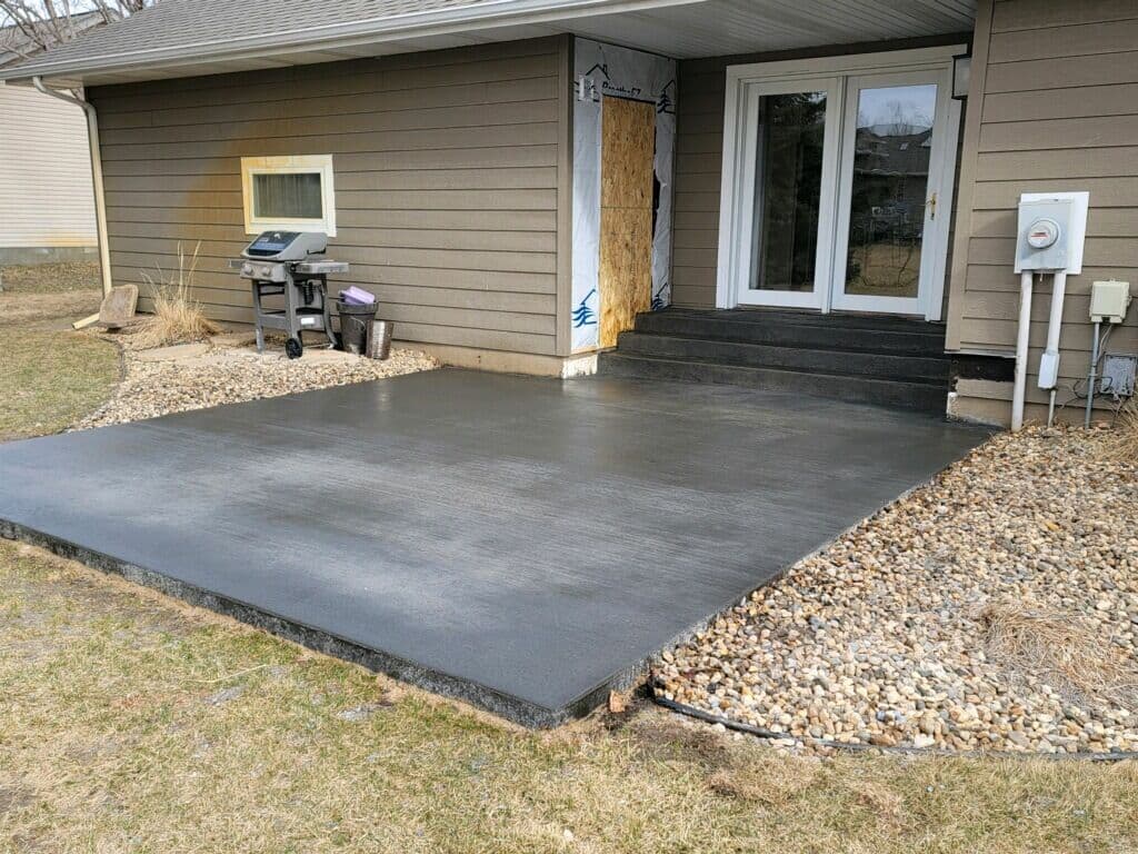 A finished backyard concrete patio and steps at a patio door