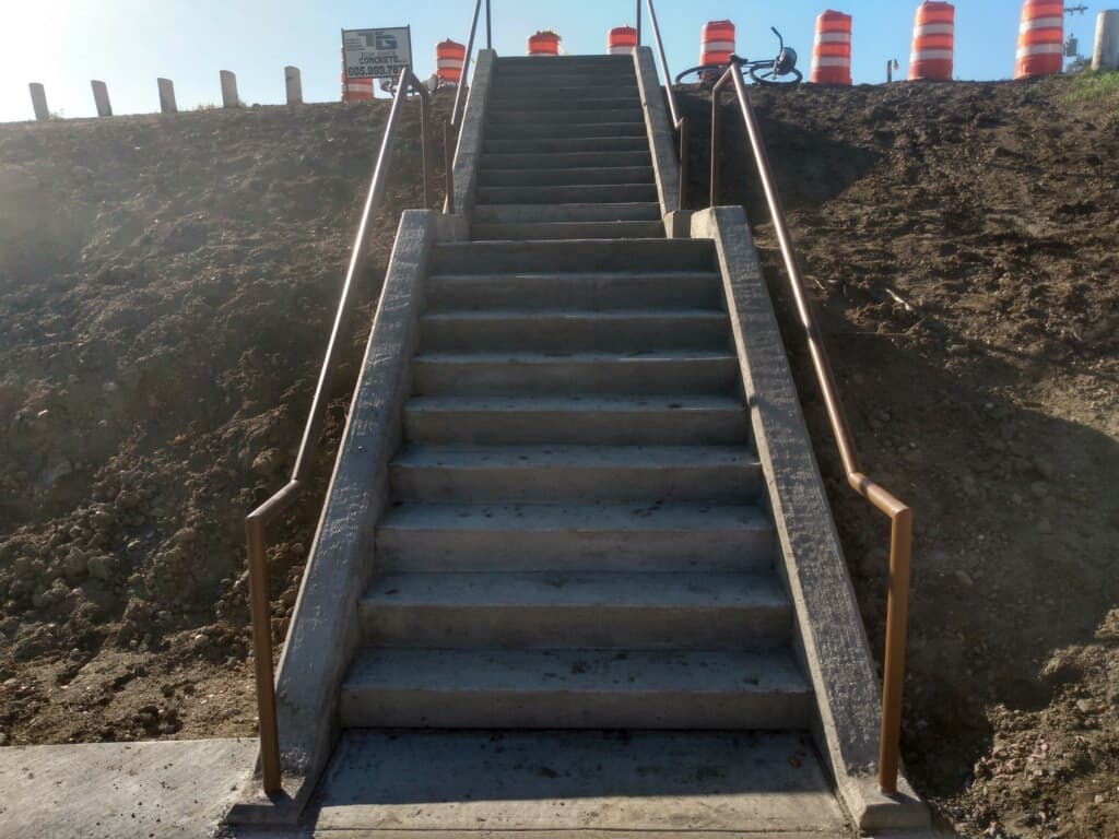 A long run of new concrete stairs with steel railings, the Top Grade jobsite sign at the top